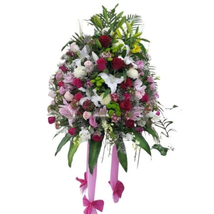 Floral Joy Stand with red and pink roses, white lilies, pink carnations, and baby’s breath, accented with lush greenery and pink ribbons for celebrations.