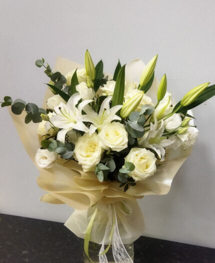 A serene bouquet featuring white roses and white lilies, elegantly wrapped with soft neutral paper, perfect for weddings or special occasions.